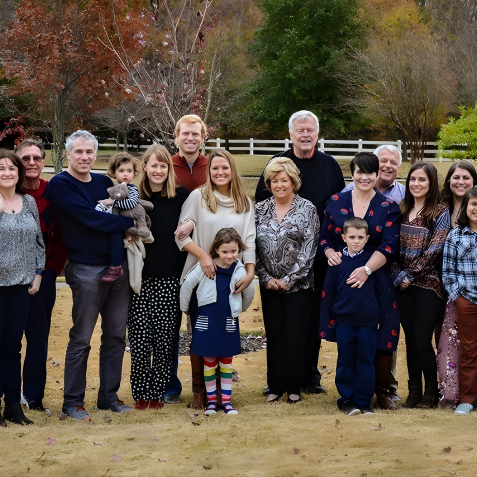 A large group, including adults and children, stands together outdoors on a lawn with trees and a white fence in the background, smiling for a Martin family group photo. It appears to be a family gathering focused on building a legacy.