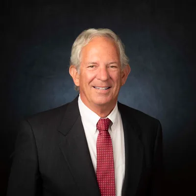 Headshot of a smiling man with grey hair wearing a dark suit and a red patterned tie, an Allied Professional Advisor attending the 2025 seminar.