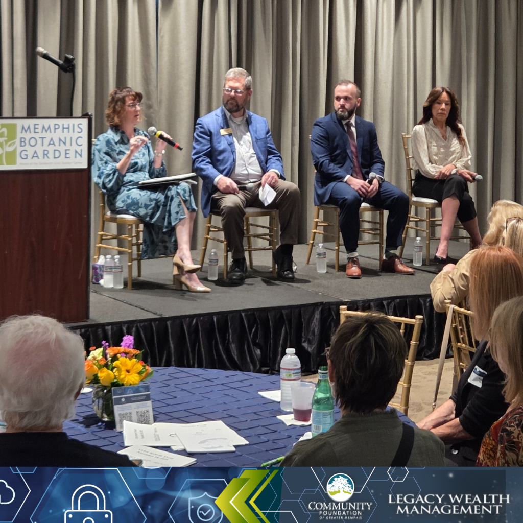Four panelists, three seated and one speaking with a microphone, discuss cybercrime onstage at Memphis Botanic Garden. Audience members watch intently, with event banners and flowers visible in the foreground.