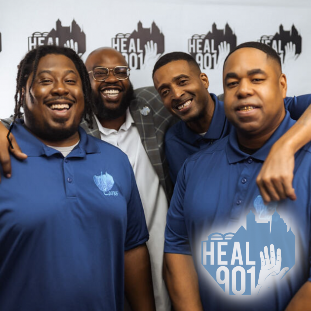 Four smiling men pose together in matching blue Heal 901 shirts, standing in front of a step-and-repeat backdrop. Their unity reflects Heal 901's commitment to youth empowerment and positive change in Memphis.