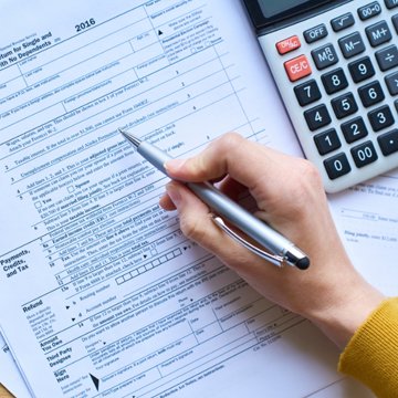 A person holding a pen fills out a tax form, with a calculator nearby on the desk.
