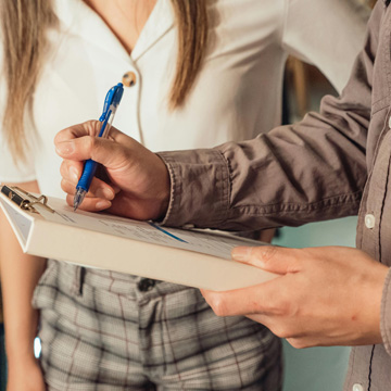 Two people standing; one holds and writes on a clipboard with a pen, while the other stands nearby, suggesting client communication during the process of transferring a private foundation. Only their torsos and arms are visible; faces are not shown.