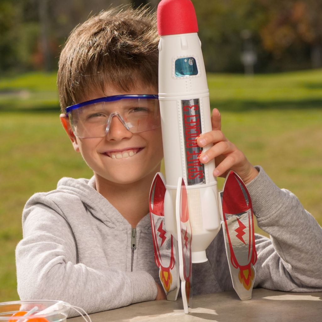 Smiling boy wearing safety goggles holds a toy rocket with red fins and lightning bolt designs, outdoors on a sunny day—reminding us how split-interest charitable gifts can launch bright futures for the next generation.