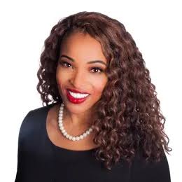 Woman with curly brown hair, wearing a black top, a pearl necklace, and red lipstick, smiling against a white background—Myra McCaskill exudes timeless elegance in this portrait.