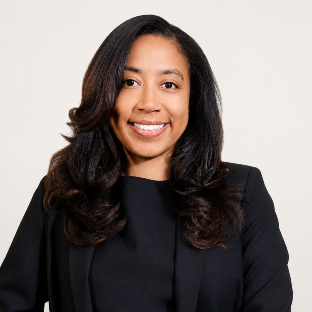 A woman with long dark hair, wearing a black blazer and top, smiles at the camera against a plain light background.