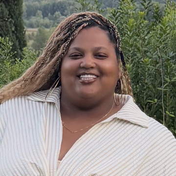 Jasmine Martin smiling with braided hair while wearing a collared, striped shirt outdoors.