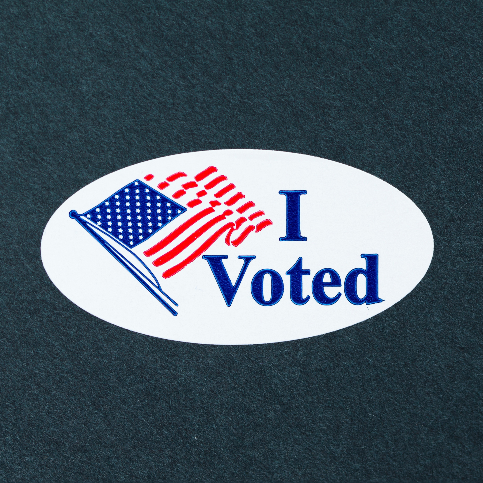 Oval sticker with an American flag and the words I Voted in blue and red text, placed on a dark background.